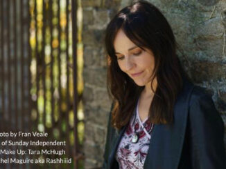 Musician annmarie cullen leaning against a wall, looking down.